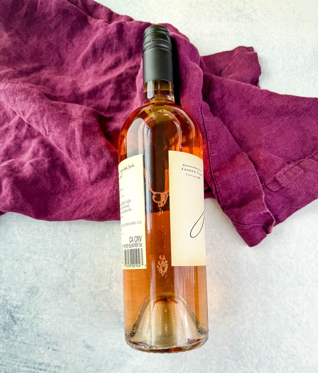 A chilled bottle of rosé wine resting on a textured white surface with a purple cloth, photographed for ingredient styling.