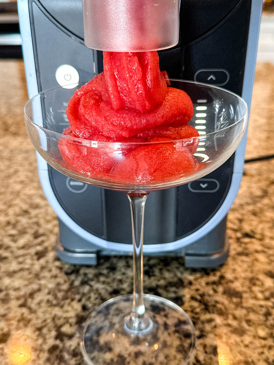 Frosé being dispensed directly into a cocktail glass from the Ninja Slushi machine, showing the machine in use.