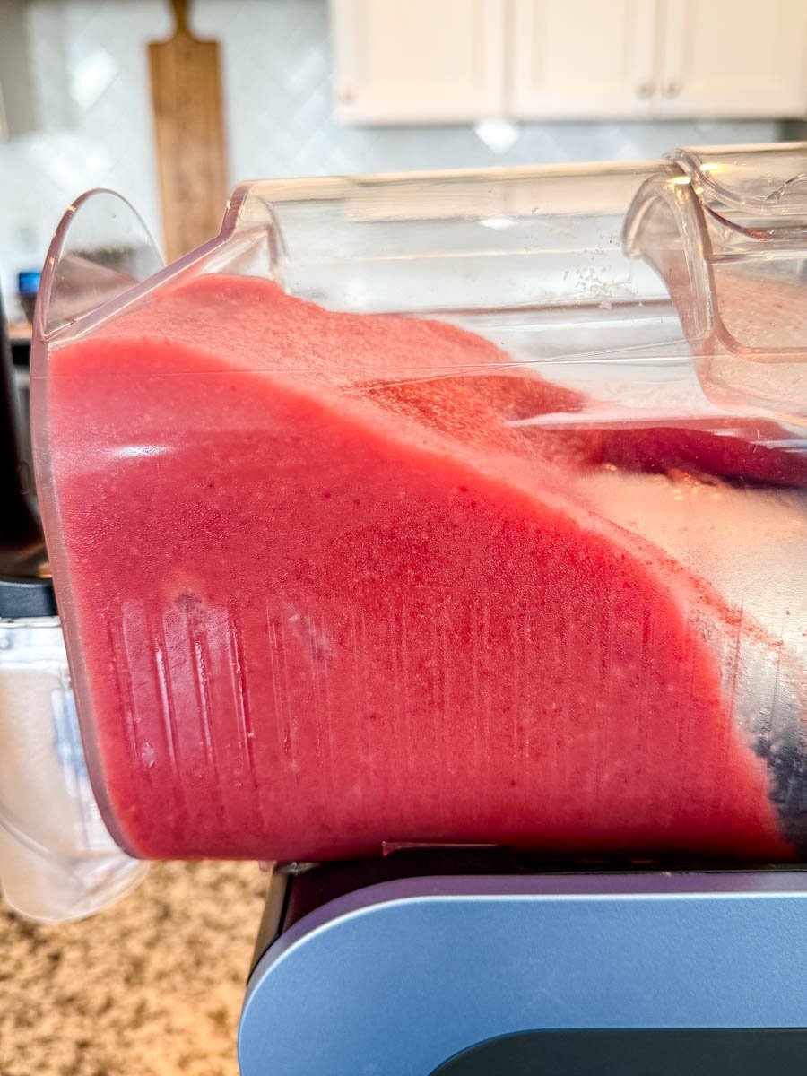 Side view of the Ninja Slushi machine in action with a pitcher of thick, red frozen frosé mixture inside.