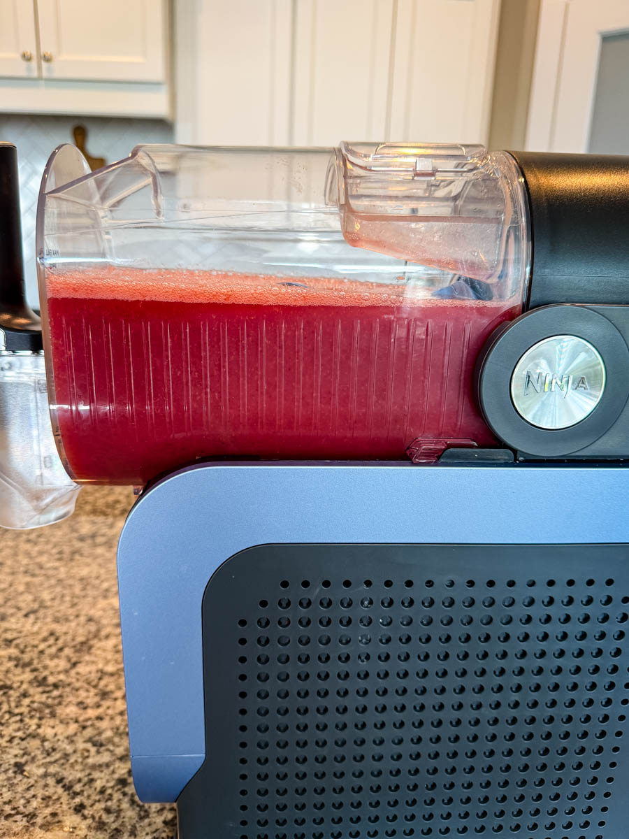 Full side shot of the Ninja Slushi machine filled with a vibrant red frosé mixture, ready to dispense.