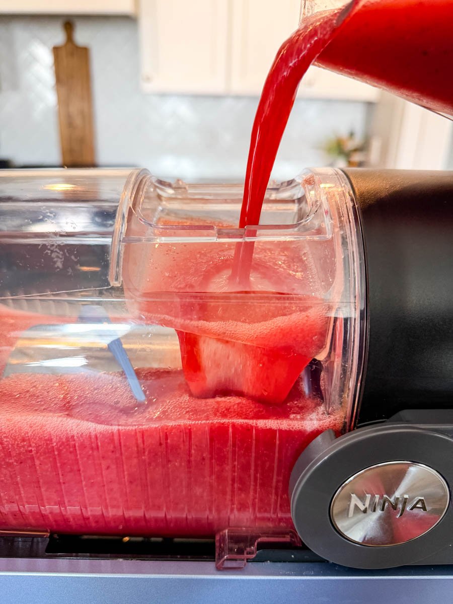 Pouring a vibrant red frosé mixture into the Ninja Slushi machine, showing the machine mid-fill with a thick, icy texture.