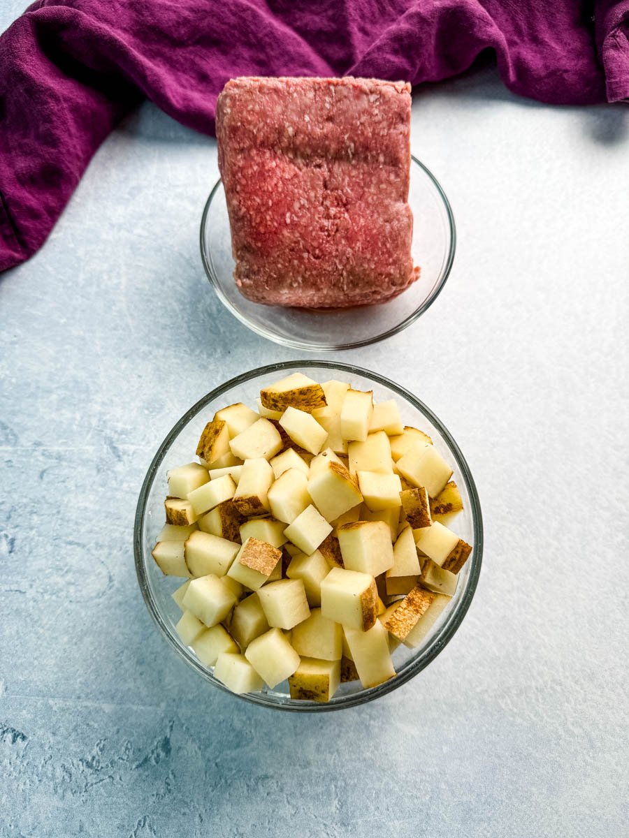 Overhead view of raw ground beef and a bowl of diced russet potatoes, ready to be cooked for a taco potato skillet recipe.