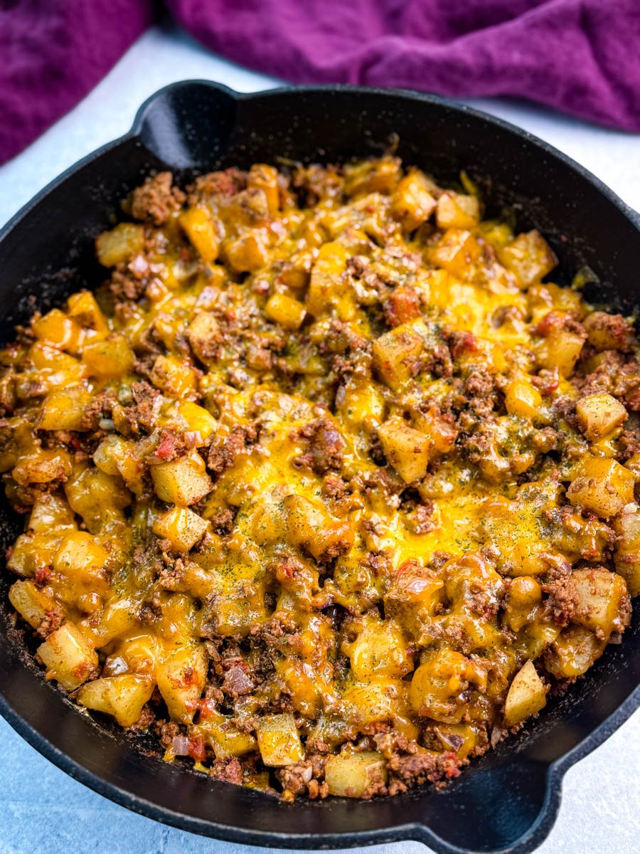 Cheesy, golden taco potatoes and seasoned ground meat cooked in a large black cast iron skillet, garnished with herbs and ready to serve.