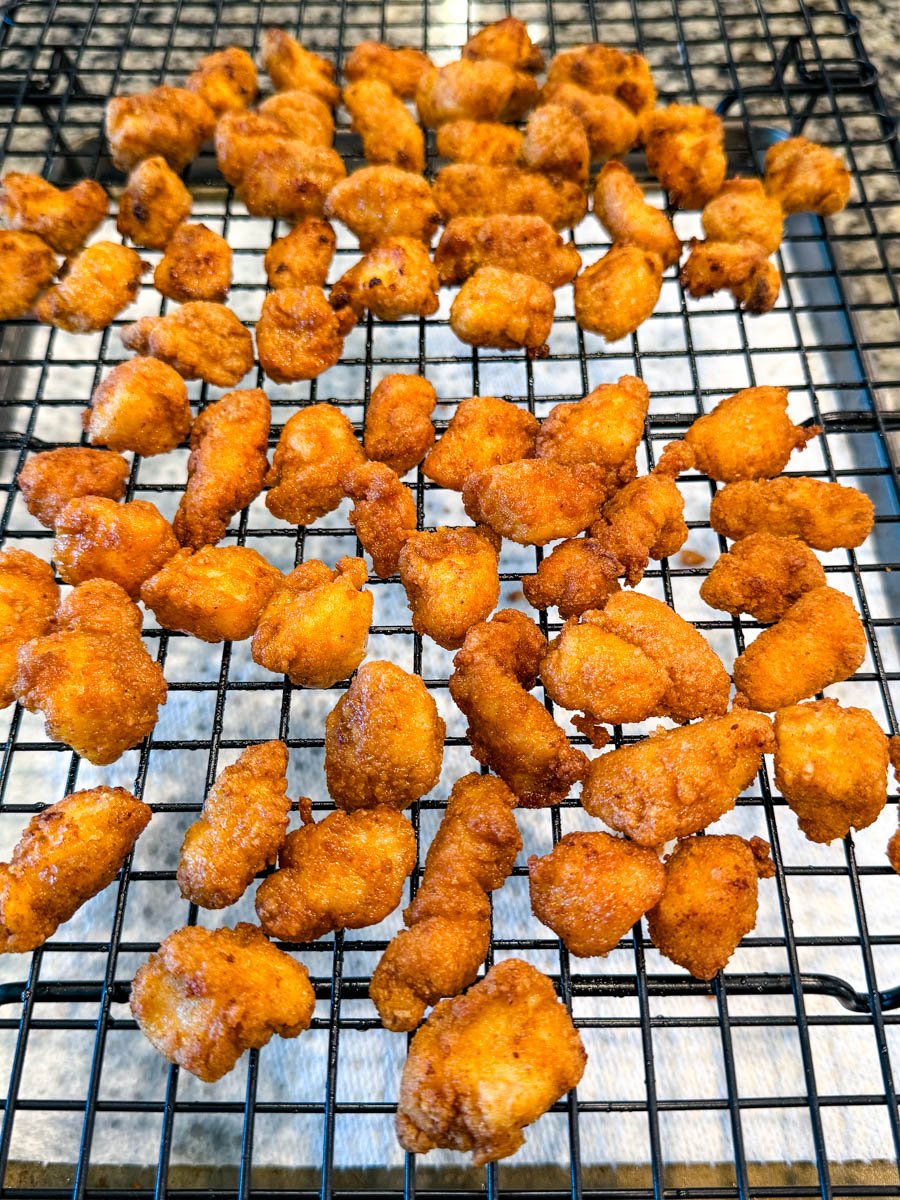 Golden brown fried chicken bites cooling on a wire rack over paper towels.