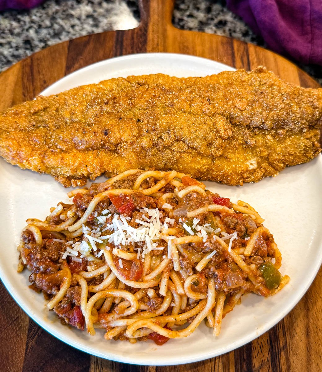 A serving plate with one large piece of fried catfish and a scoop of spaghetti topped with shredded Parmesan cheese.