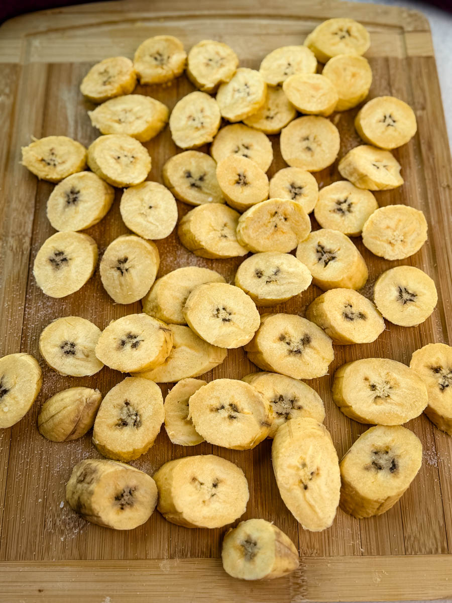 Raw, sliced plantains arranged in a single layer in an air fryer basket before cooking.
