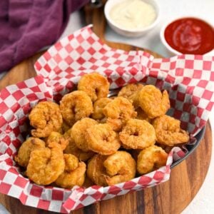 Red and white checkered basket brimming with breaded fried shrimp, photographed at an angle to highlight texture and quantity.