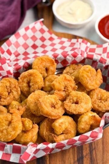 Red and white checkered basket brimming with breaded fried shrimp, photographed at an angle to highlight texture and quantity.