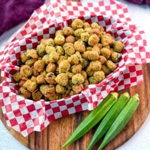 Overhead shot of Southern fried okra served in a red-checkered basket with fresh whole okra laid beside it.
