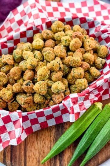 Overhead shot of Southern fried okra served in a red-checkered basket with fresh whole okra laid beside it.