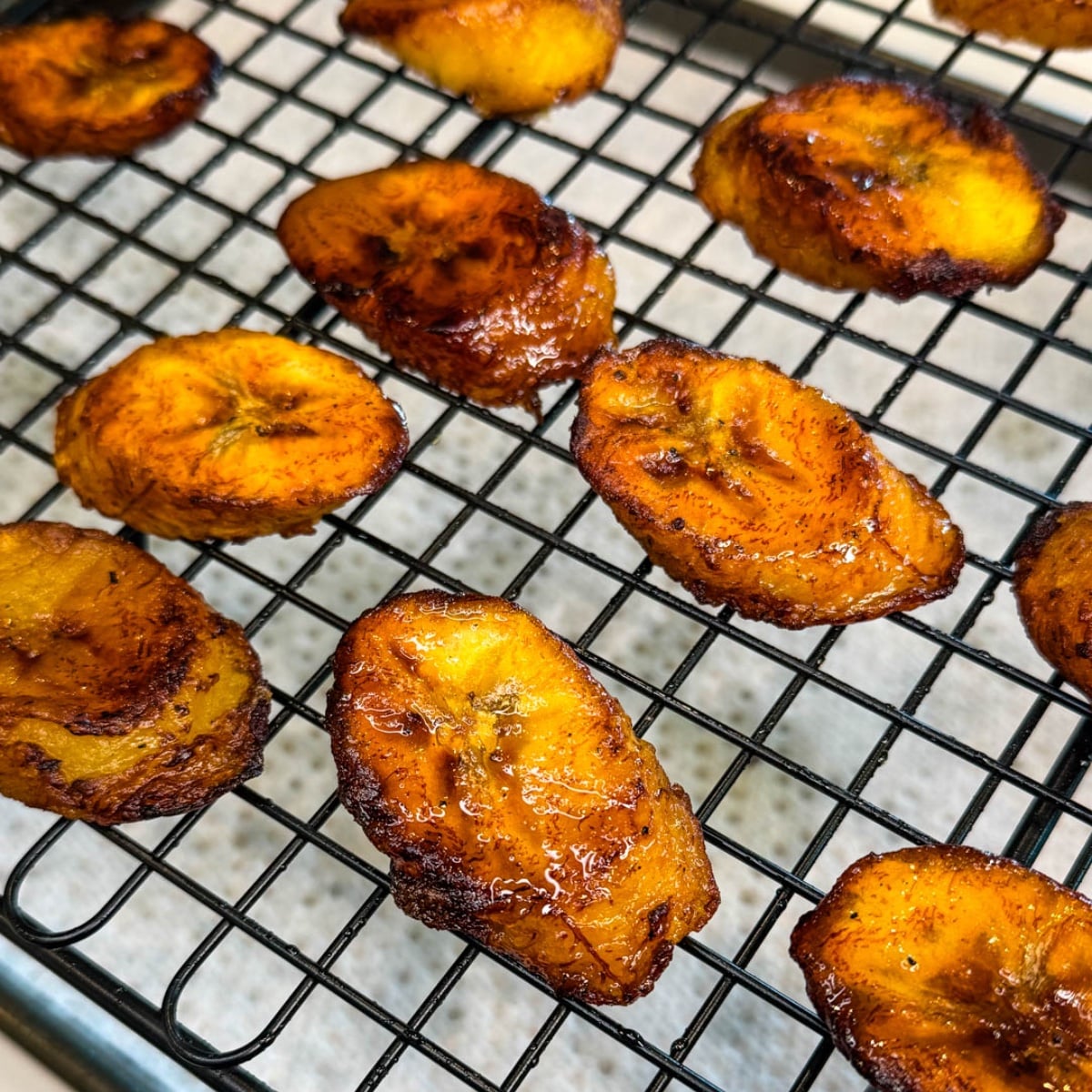 Fried sweet plantains cooling on a wire rack with crispy edges and caramelized surface