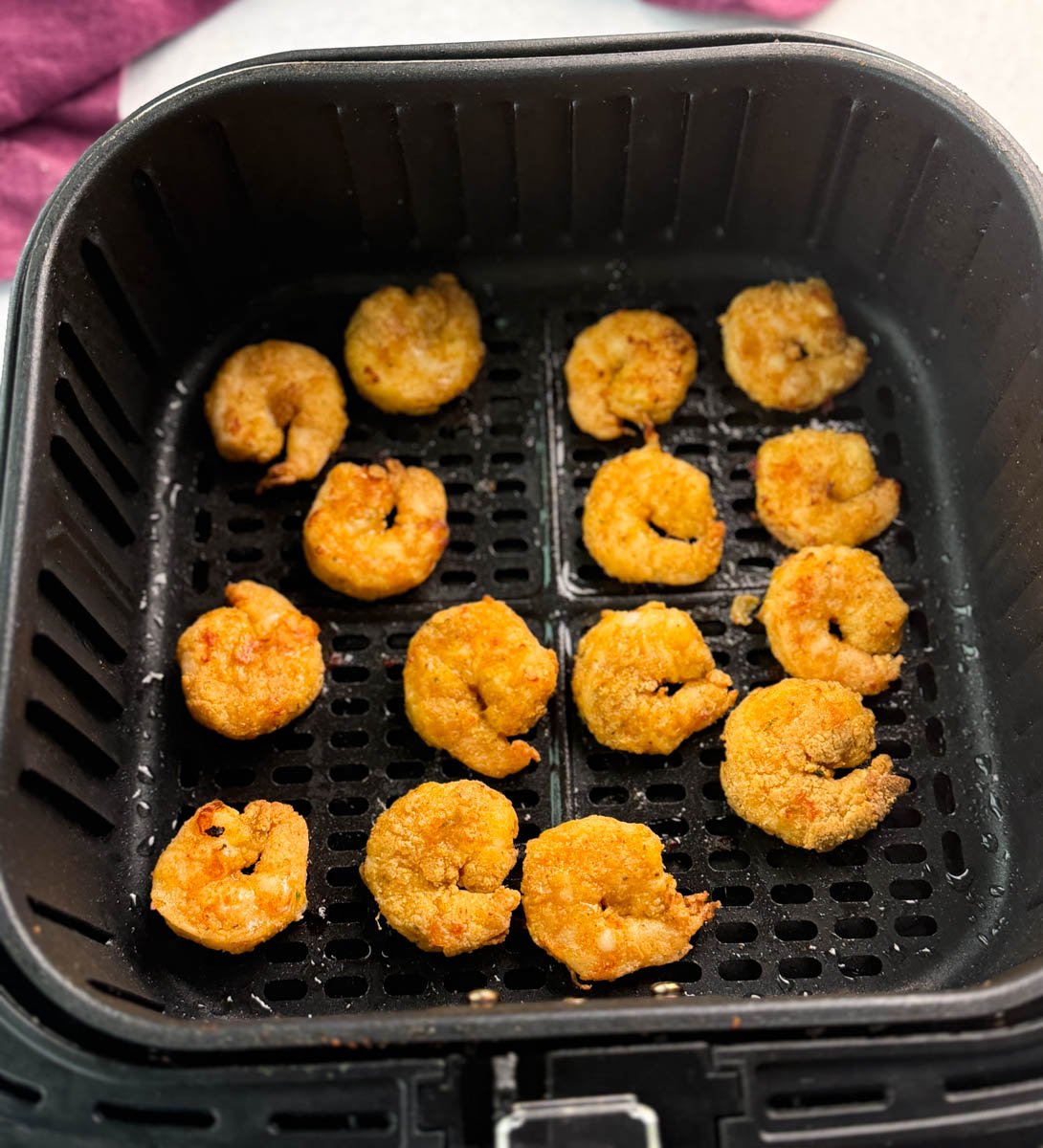 Golden breaded shrimp arranged inside an air fryer basket, freshly cooked and ready to serve.