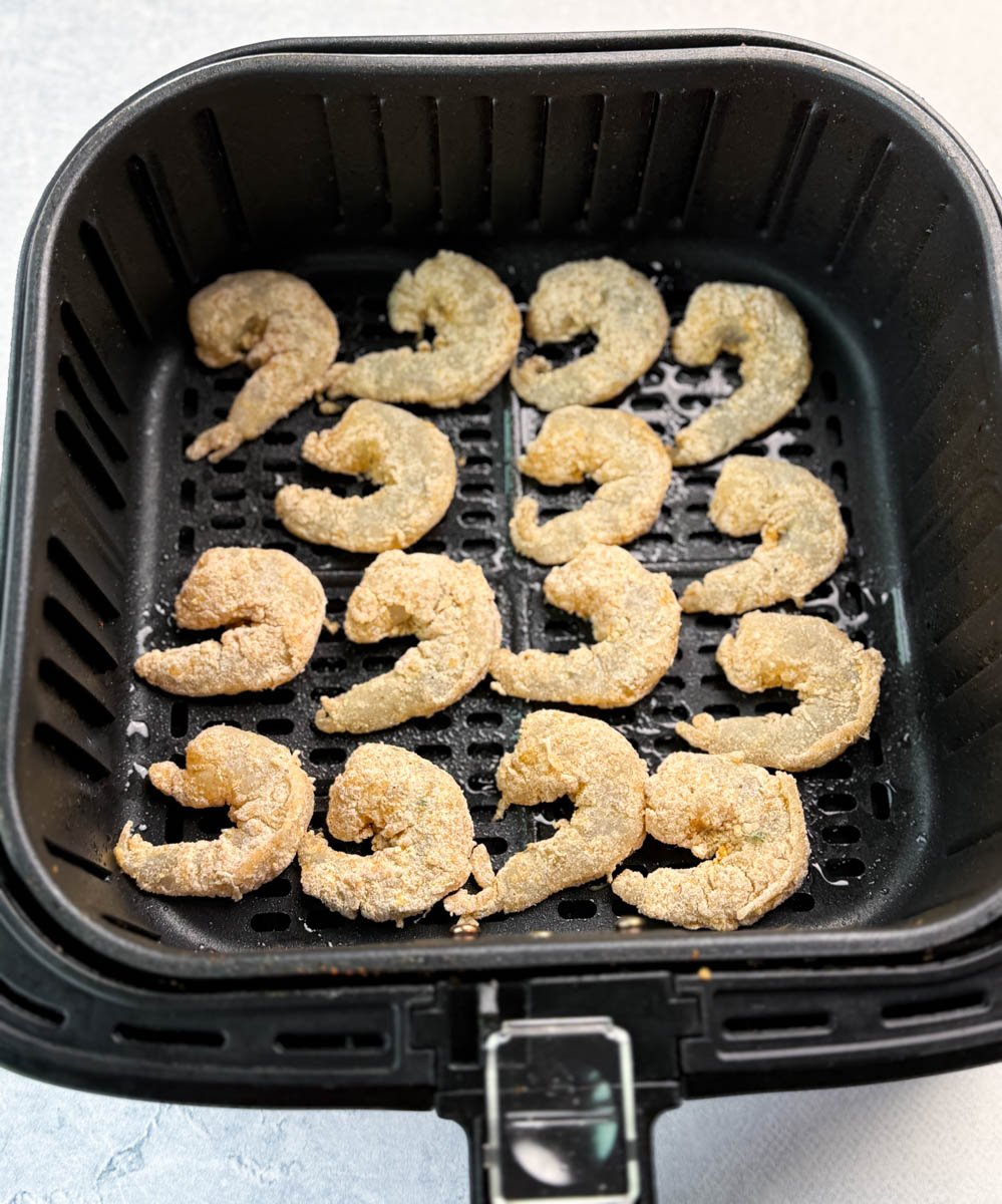 Raw breaded shrimp arranged neatly in an air fryer basket before cooking.