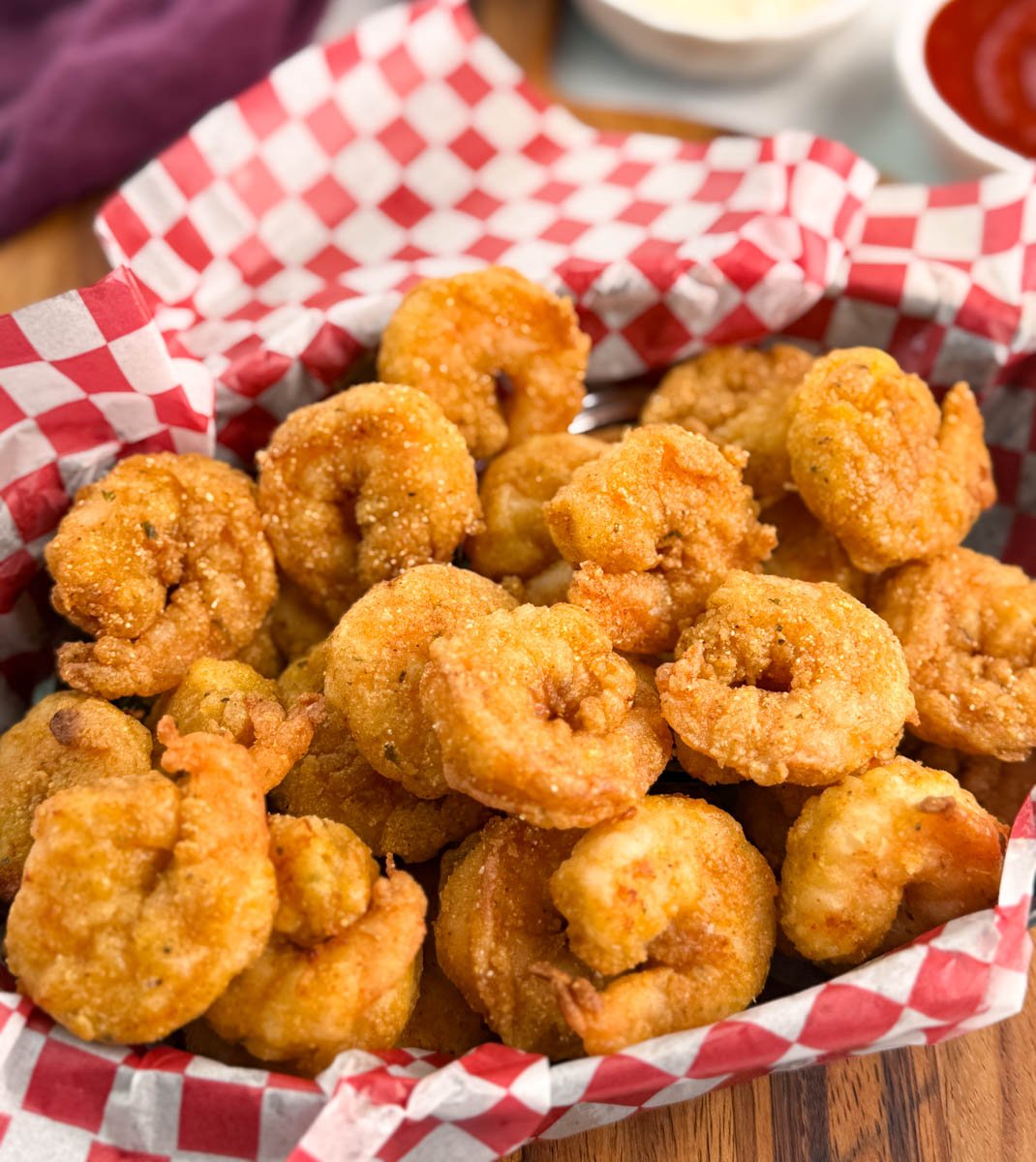 Wide-angle view of the shrimp basket on a round wooden board, surrounded by tartar sauce, cocktail sauce, and a folded purple cloth napkin.