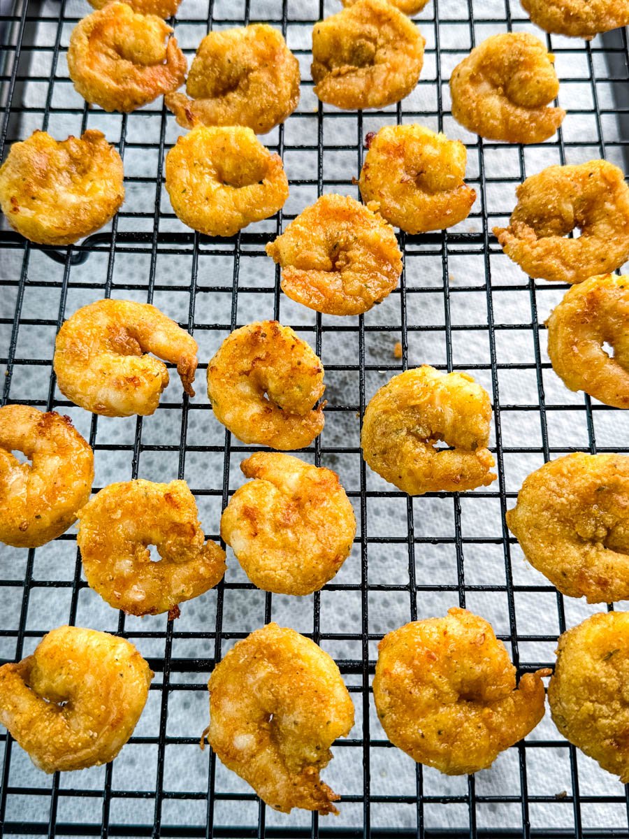 Crispy breaded shrimp cooling on a wire rack after frying, spaced evenly to preserve crispness.