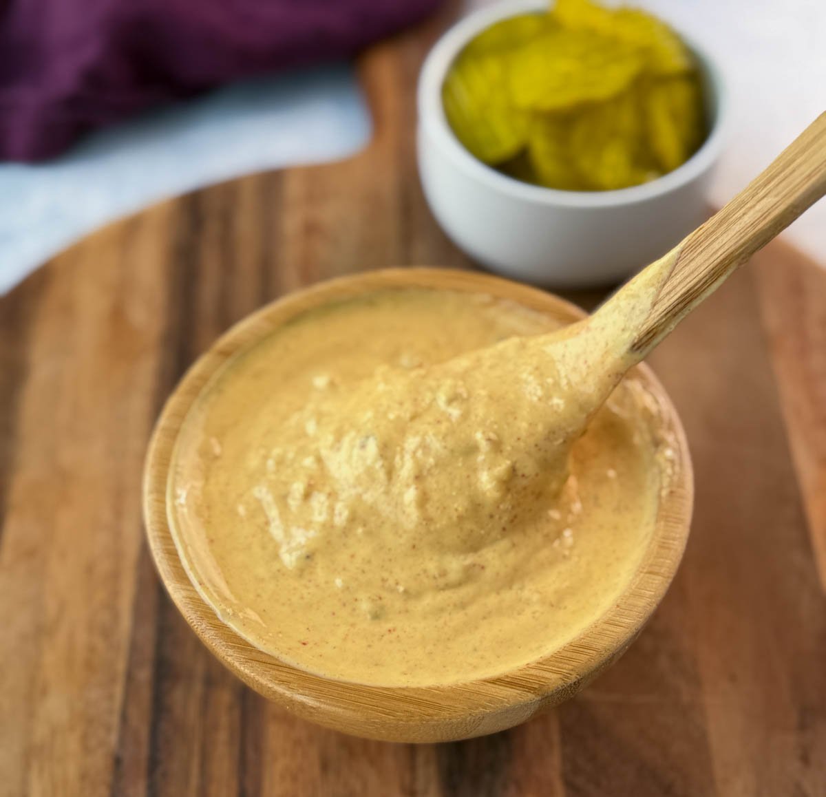 Close-up of a spoon lifting and drizzling Big Mac sauce from a wooden bowl on a wooden cutting board.