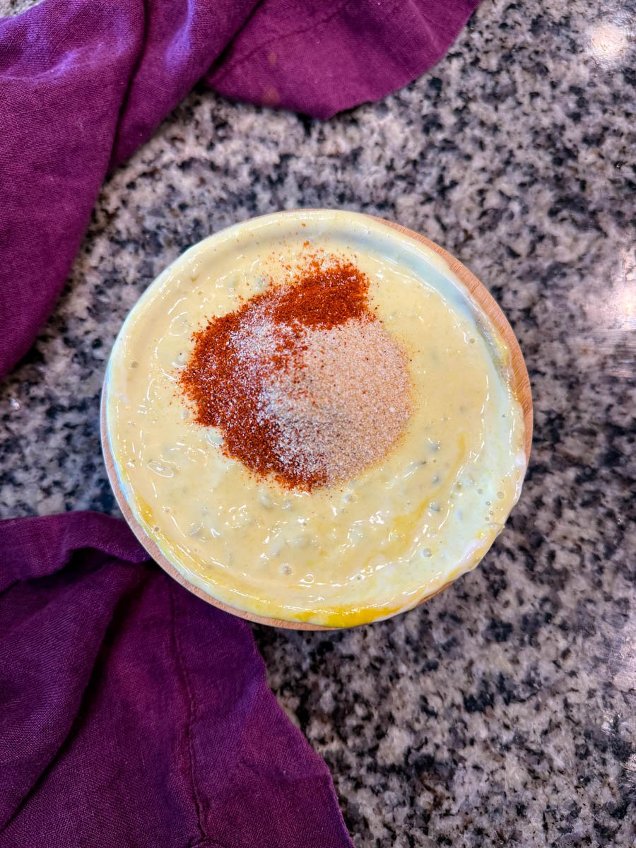 Top-down view of a bowl of Big Mac sauce with paprika, garlic powder, and onion powder sprinkled on top, next to a purple napkin.