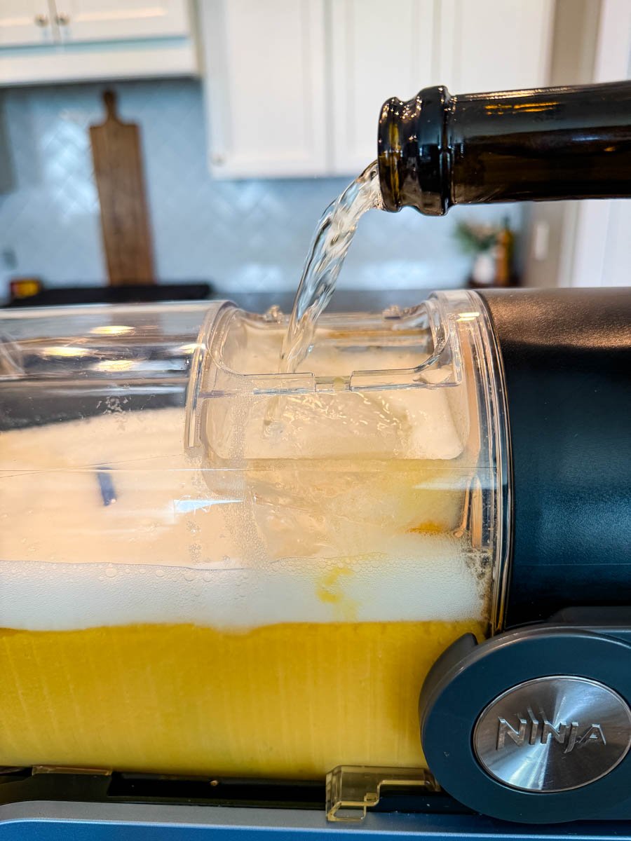 Prosecco being poured into the Ninja Slushi container filled with a peach mixture.