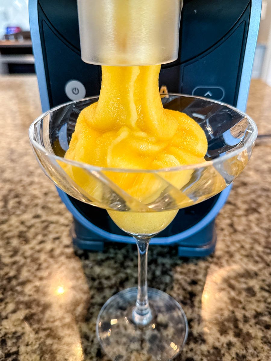 Frozen peach bellini dispensing into a cocktail glass from the Ninja Slushi machine spout.