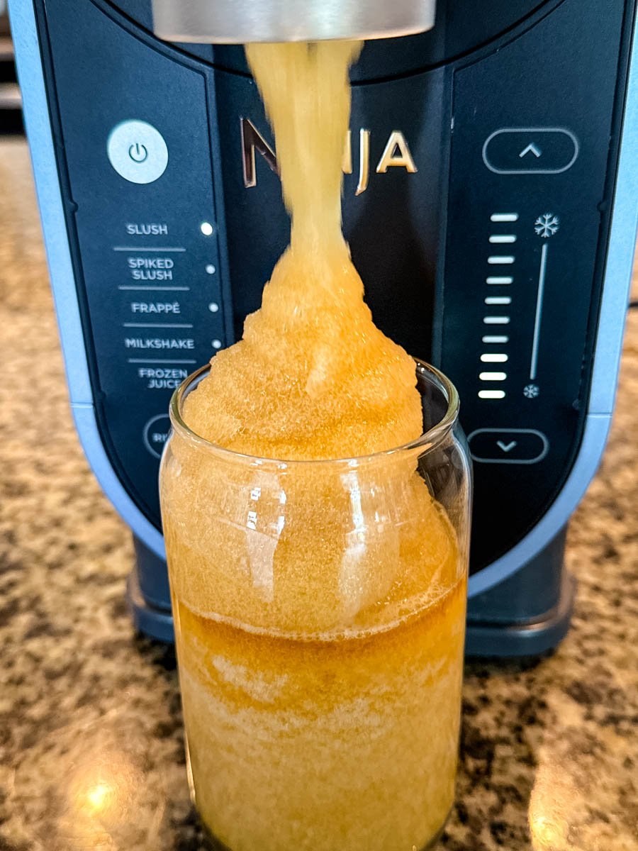 The Ninja Slushi machine dispensing a mound of iced tea slush into a clear glass.