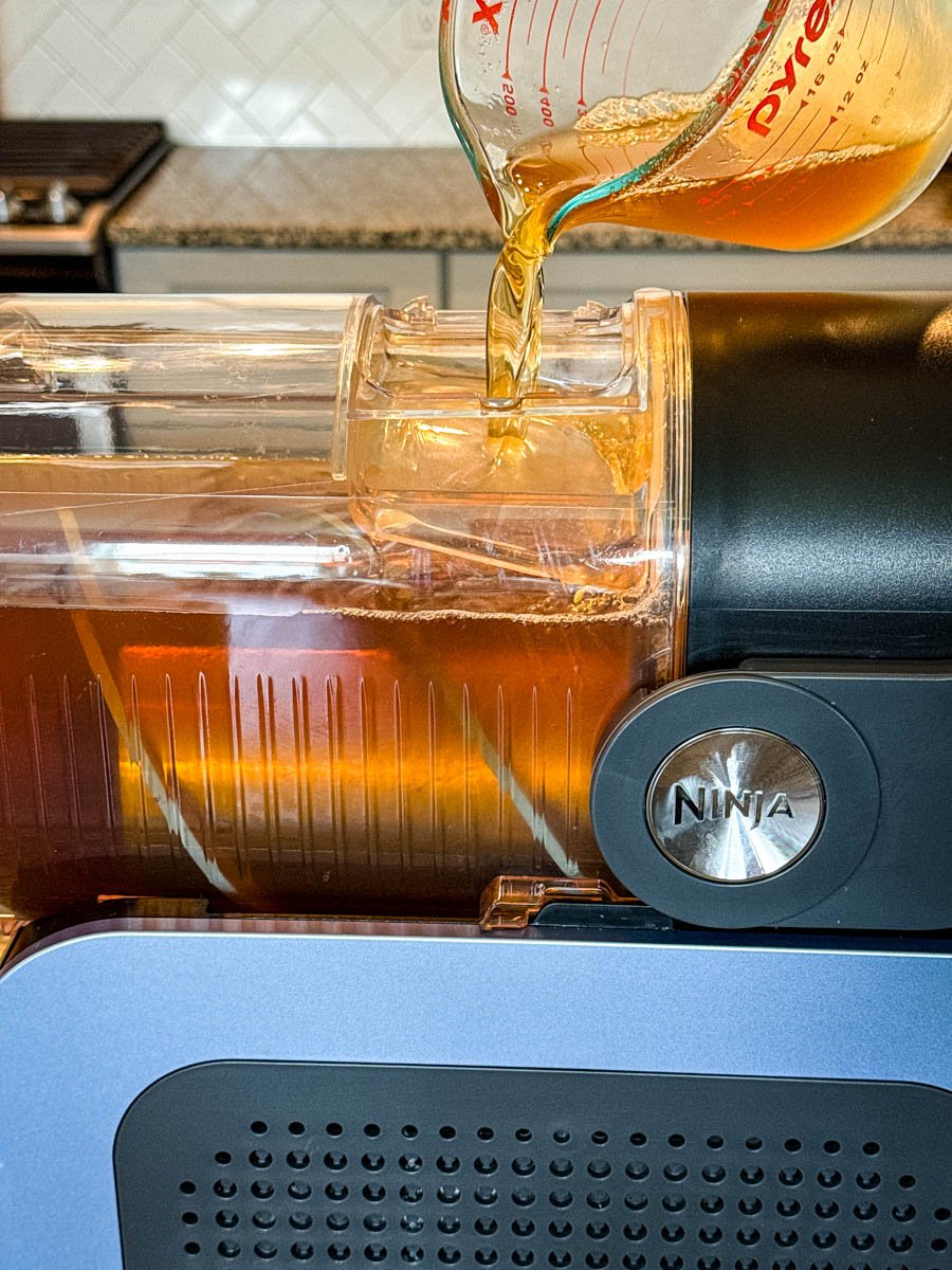 Iced tea being poured from a glass measuring cup into the Ninja Slushi machine's chamber.