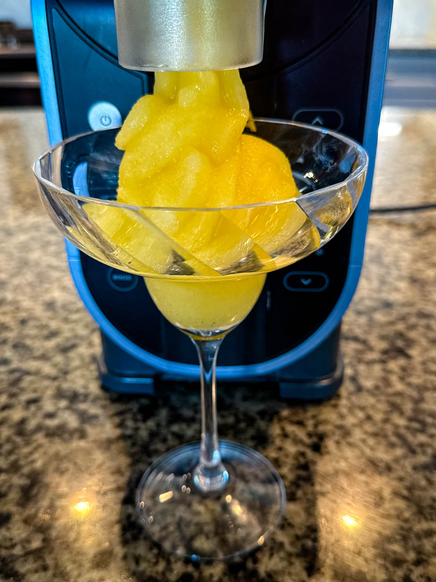 Bright yellow frozen mimosa being dispensed into a coupe glass from the Ninja Slushi machine.