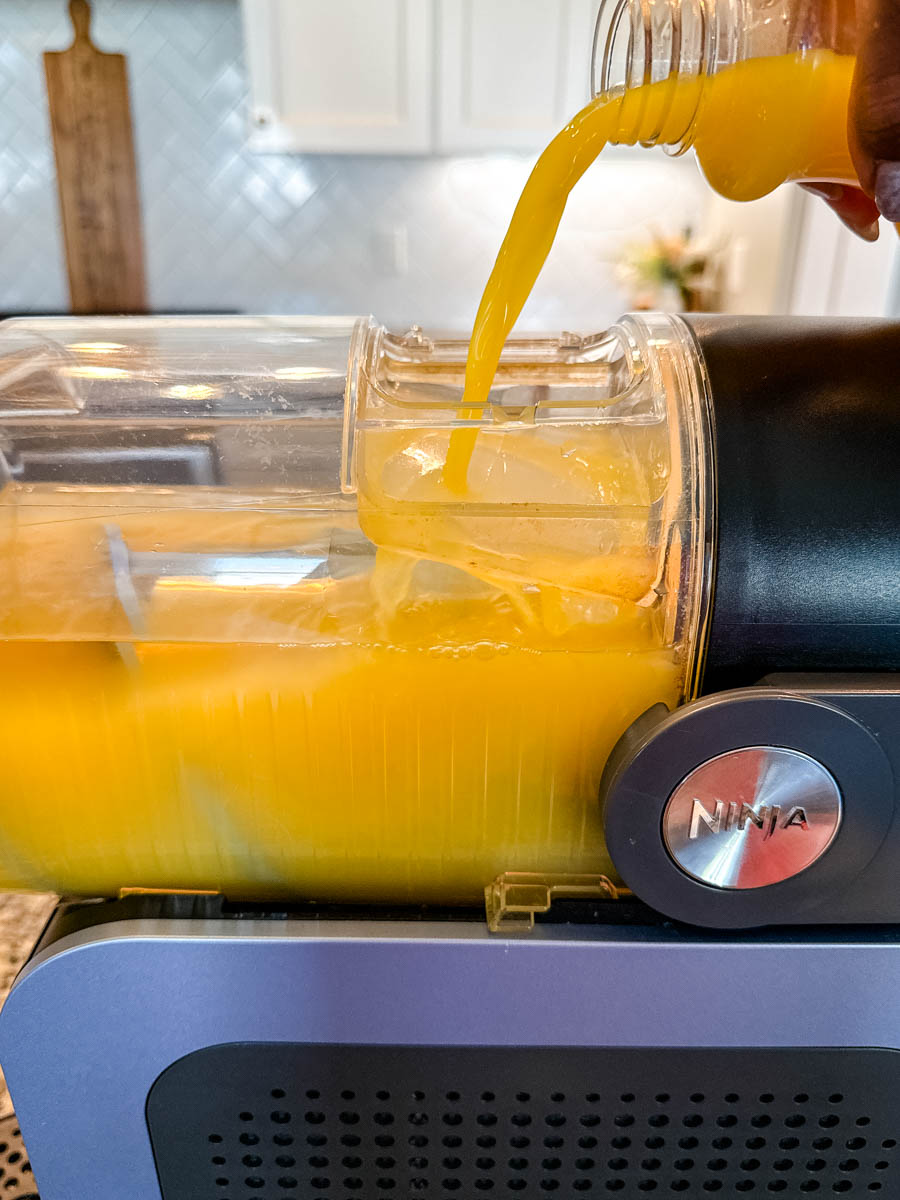 Bright orange juice being poured into the machine over the ice.
