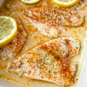 Alternate angle of garlic Parmesan baked flounder fillets in a white baking dish with lemon rounds and herbs on top.