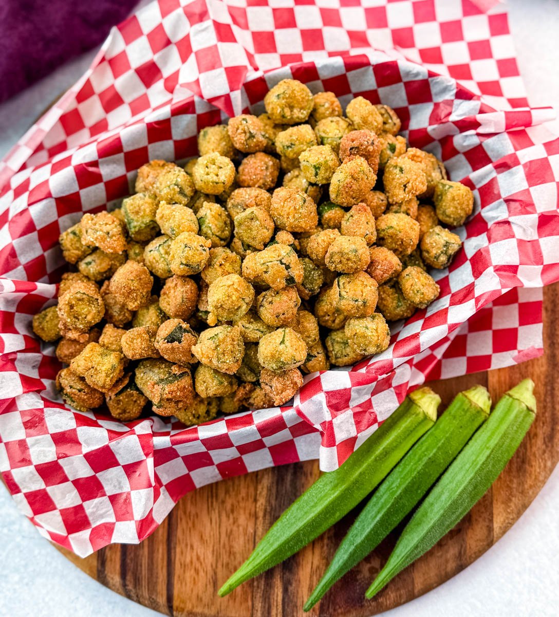 Overhead shot of Southern fried okra served in a red-checkered basket with fresh whole okra laid beside it.