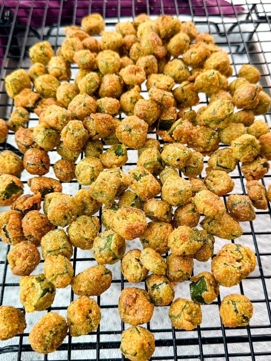 Dozens of golden brown fried okra pieces cooling on a wire rack after frying, evenly spaced and perfectly crisp.