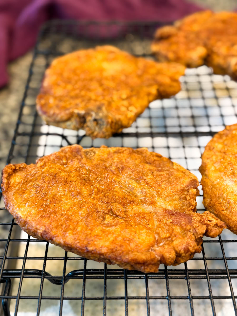 Close-up shot of crispy golden pork chops on a wire rack after frying.