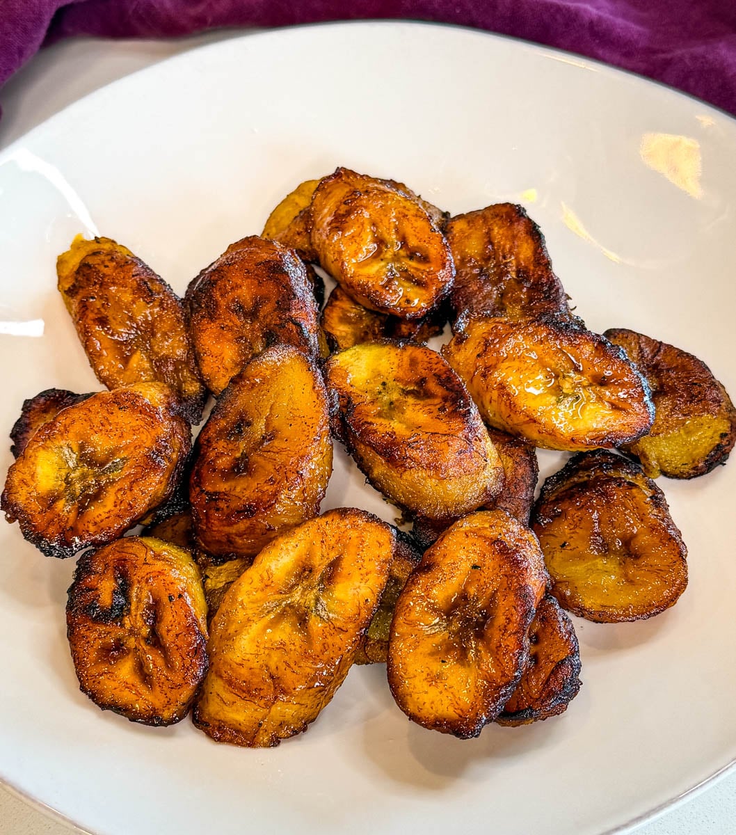 Golden brown sweet fried plantains on a white plate with caramelized edges and a glossy finish