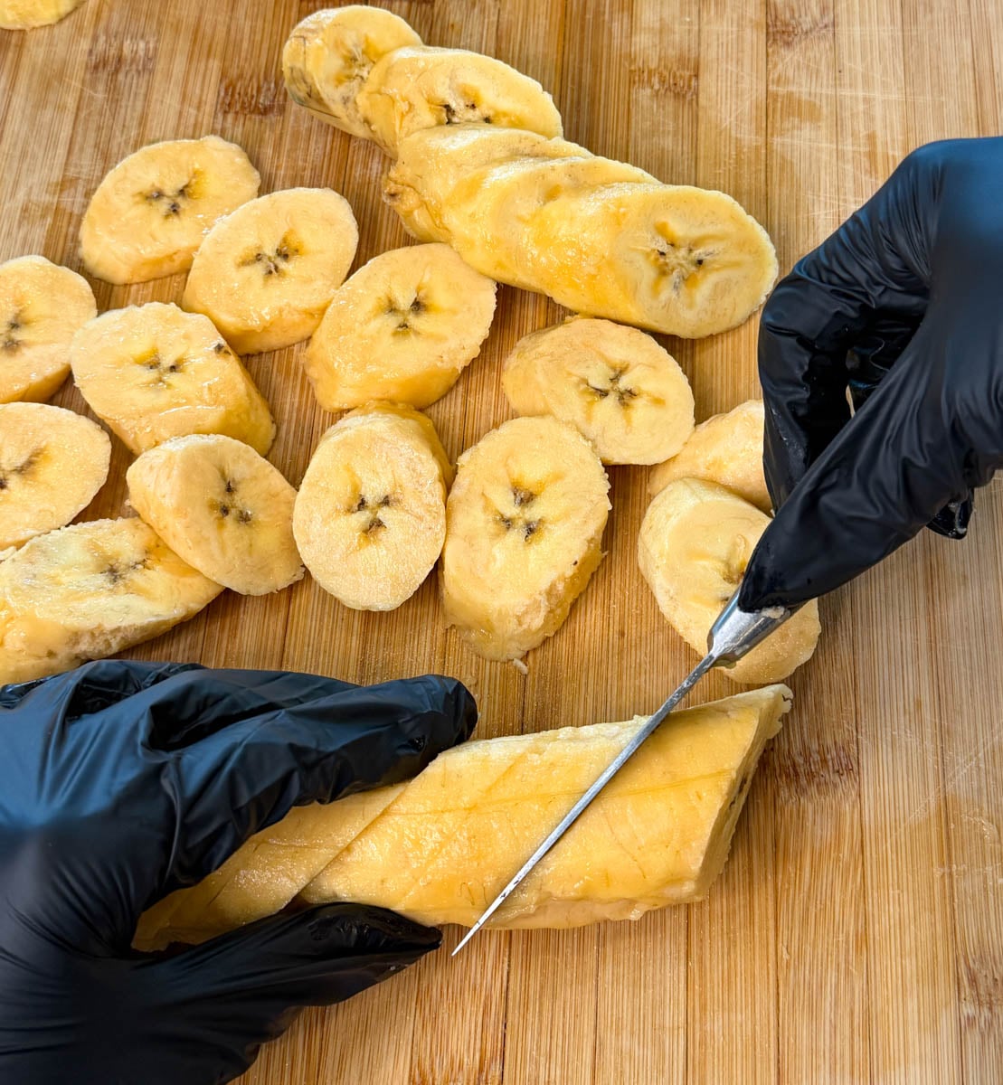 Hands slicing a peeled ripe plantain into diagonal pieces on a wooden cutting board