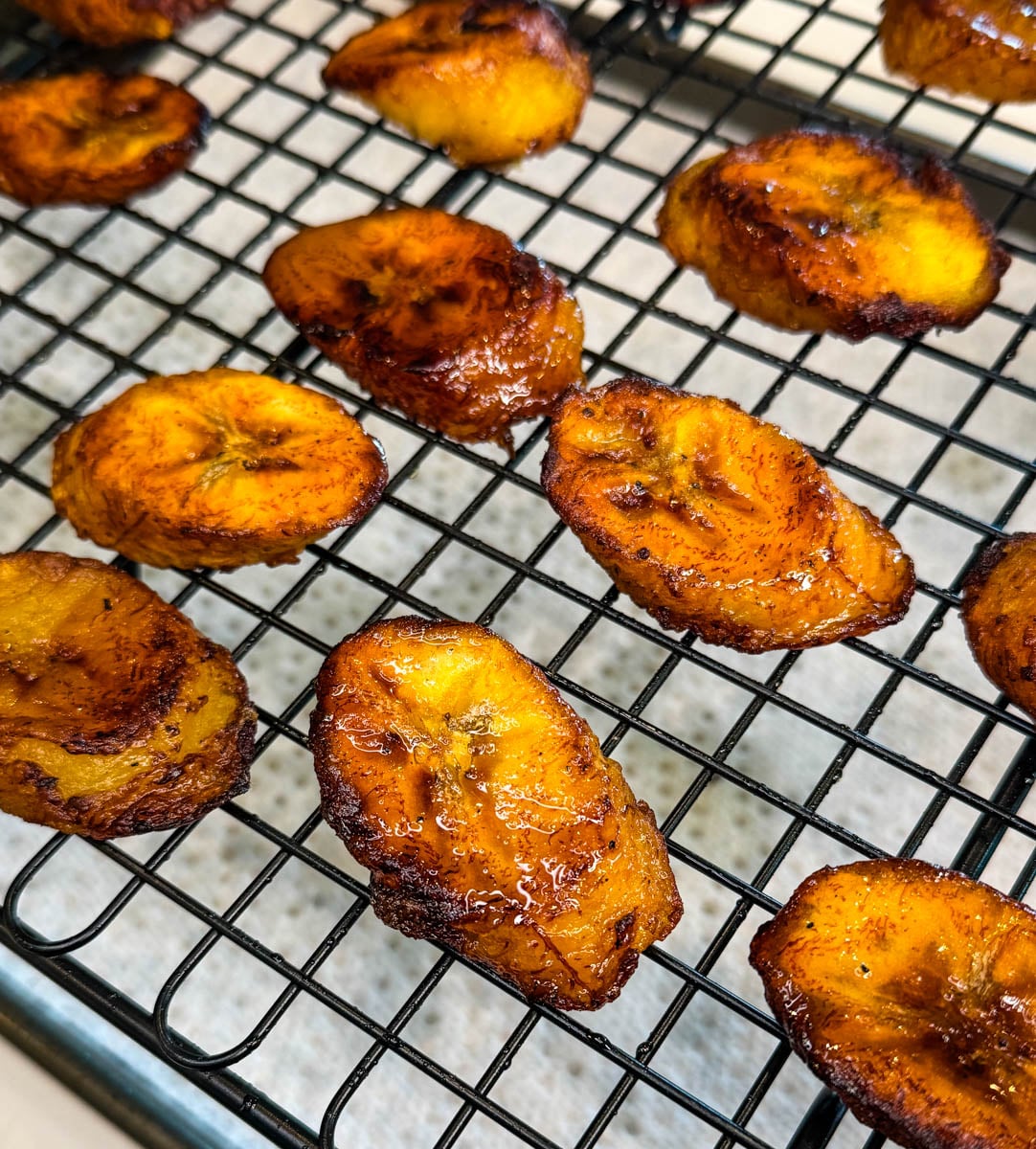 Fried sweet plantains cooling on a wire rack with crispy edges and caramelized surface