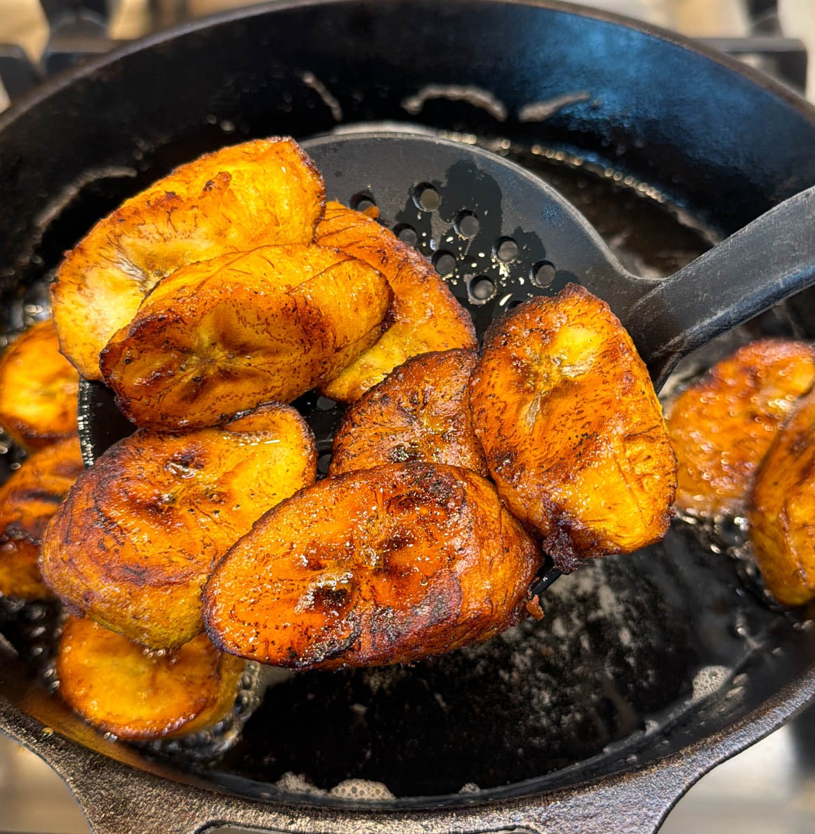 Close-up of fried plantains being lifted from hot oil with a slotted spatula