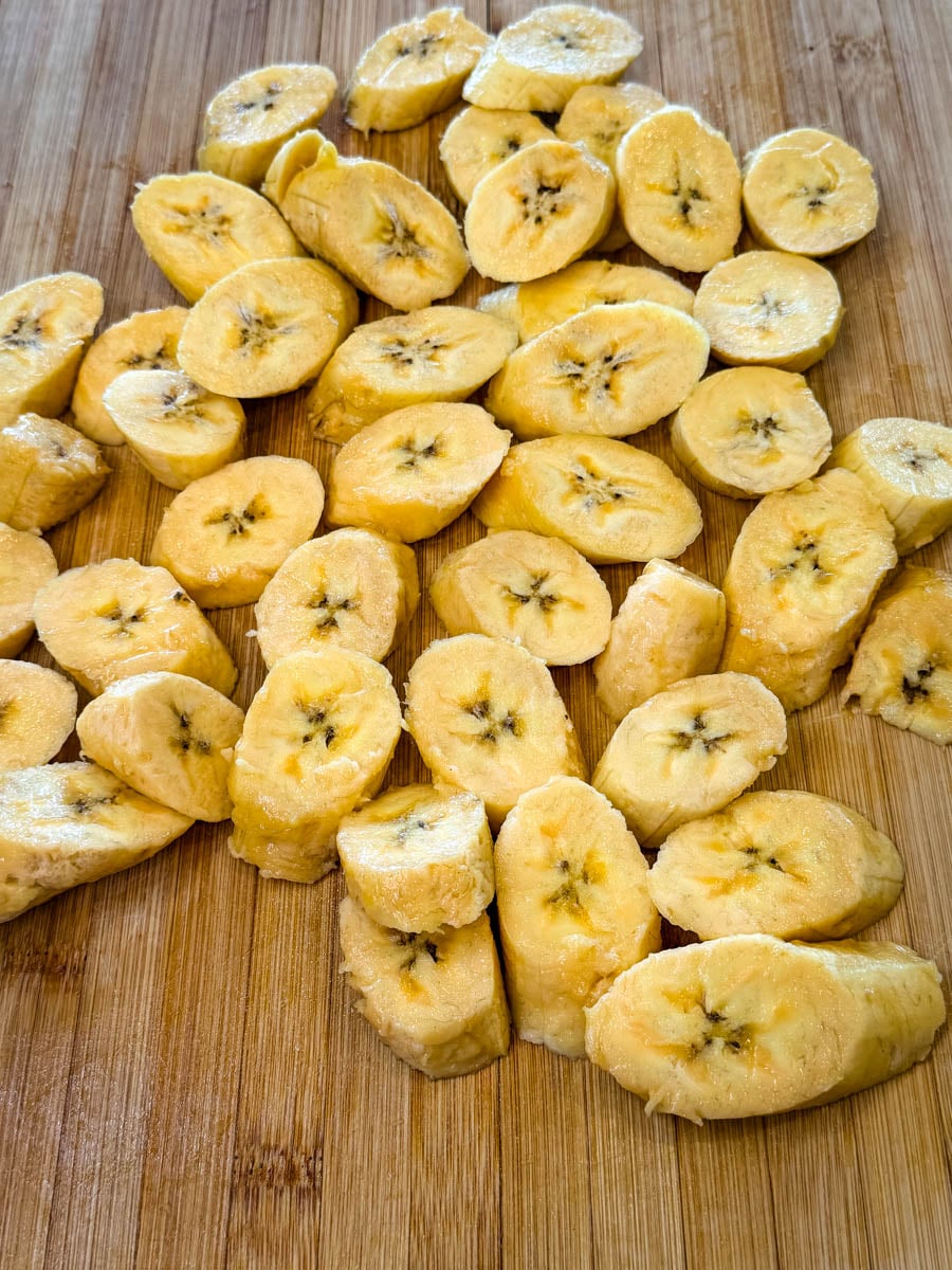 Sliced ripe plantains cut into thick rounds on a wooden cutting board