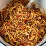 Large Dutch oven filled with Southern-style spaghetti, with a wooden spoon resting in the rich meat sauce.