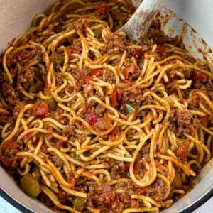 Large Dutch oven filled with Southern-style spaghetti, with a wooden spoon resting in the rich meat sauce.