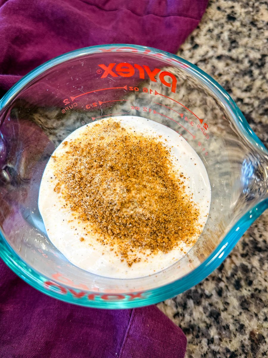A bowl of creamy ranch dressing with a generous sprinkle of Creole seasoning on top, ready to be mixed.