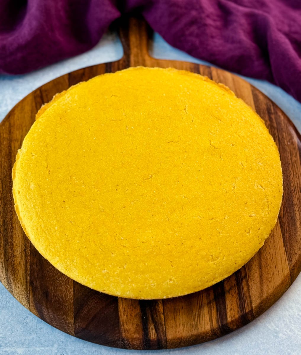 A golden round of freshly baked cornbread resting on a wooden board before slicing.