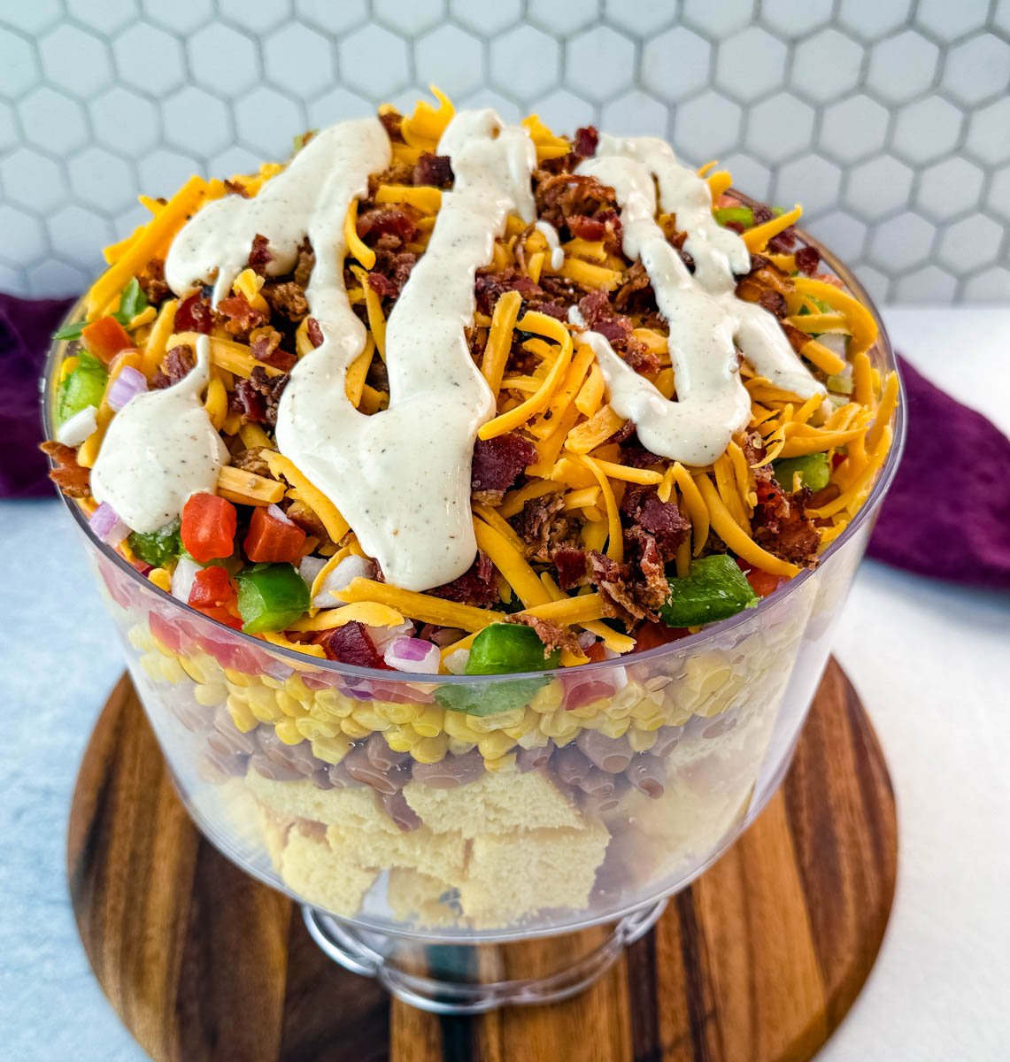 Close-up view of the top of the salad, showing shredded cheddar, chopped bacon, and thick ranch dressing drizzled across the surface.