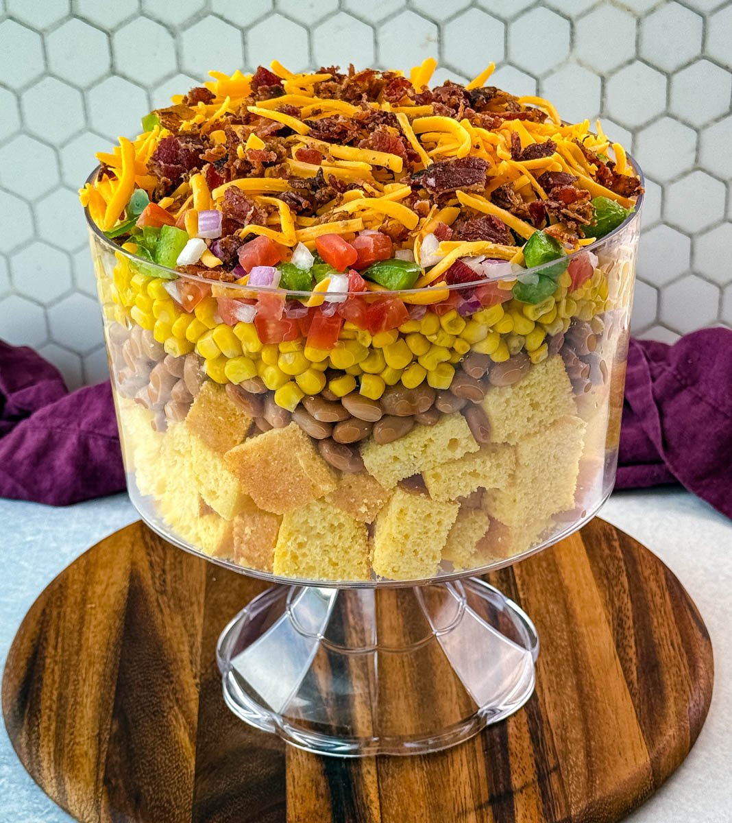 A full view of the complete Southern cornbread salad beautifully layered in a clear trifle bowl on a wooden serving board.