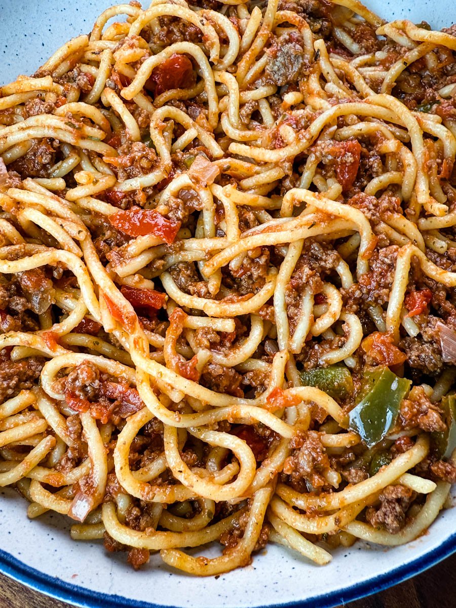 Close-up of Southern spaghetti showing tender noodles coated in a seasoned meat sauce with chunks of tomatoes and bell peppers.