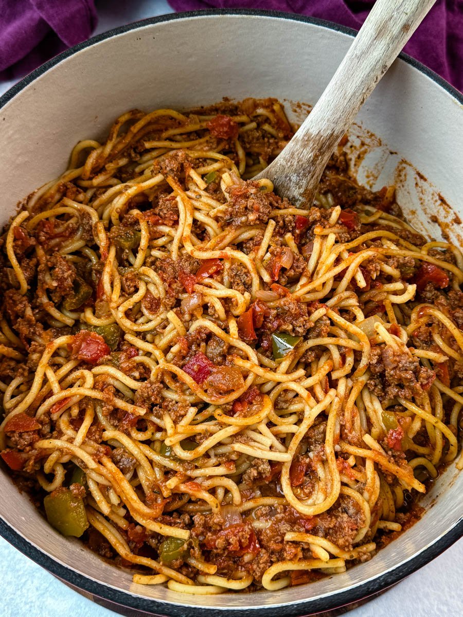Large Dutch oven filled with Southern-style spaghetti, with a wooden spoon resting in the rich meat sauce.