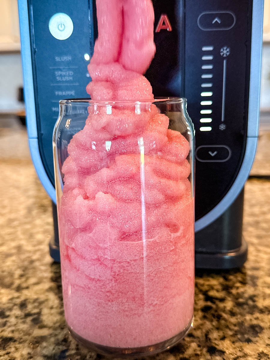 The pink fruit punch slush being dispensed from the Ninja Slushi machine into a clear glass, creating tall, swirled layers.