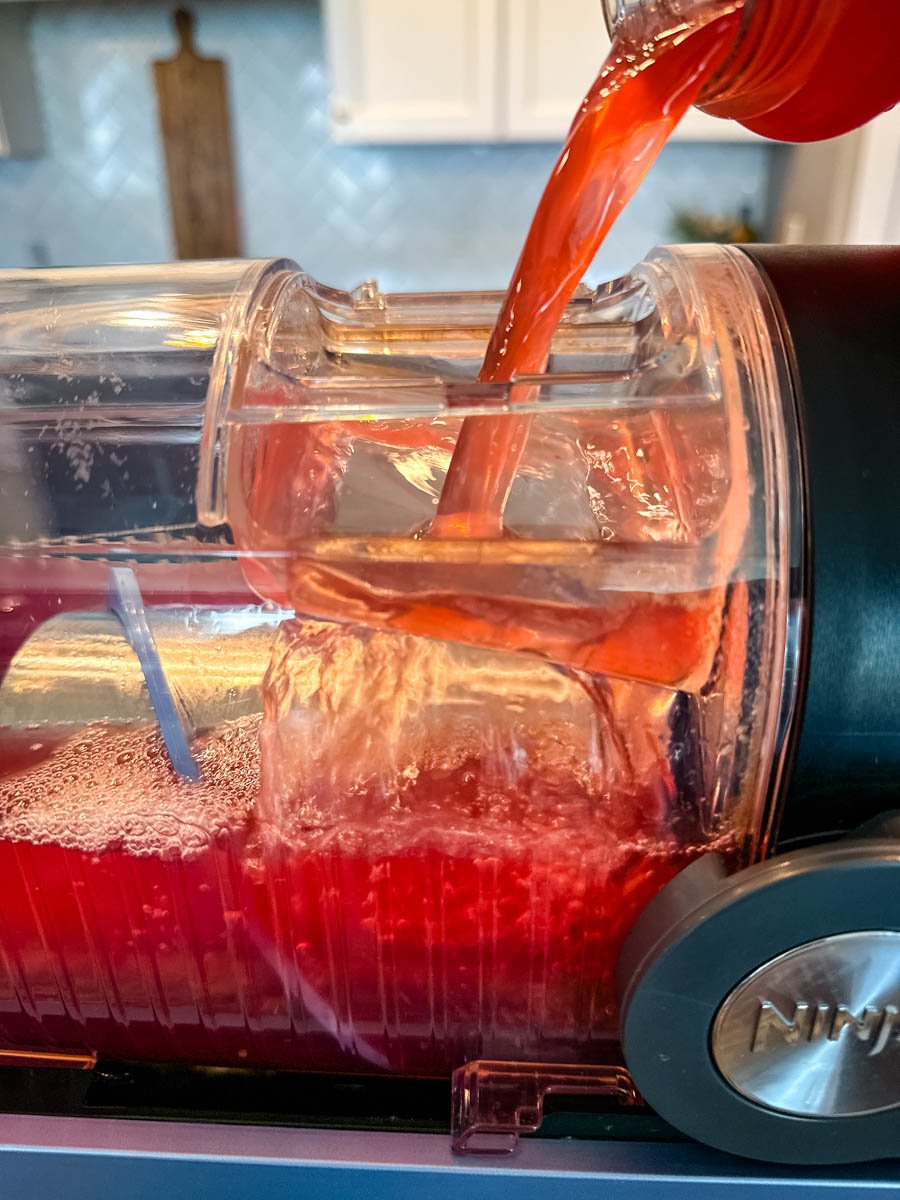 Close-up of fruit punch being poured into the Ninja Slushi machine, showing the red liquid flowing into the clear container filled with ice.