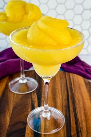 Two frozen mimosas in coupe glasses sitting on a wooden board with a hexagon tile backsplash in the background.