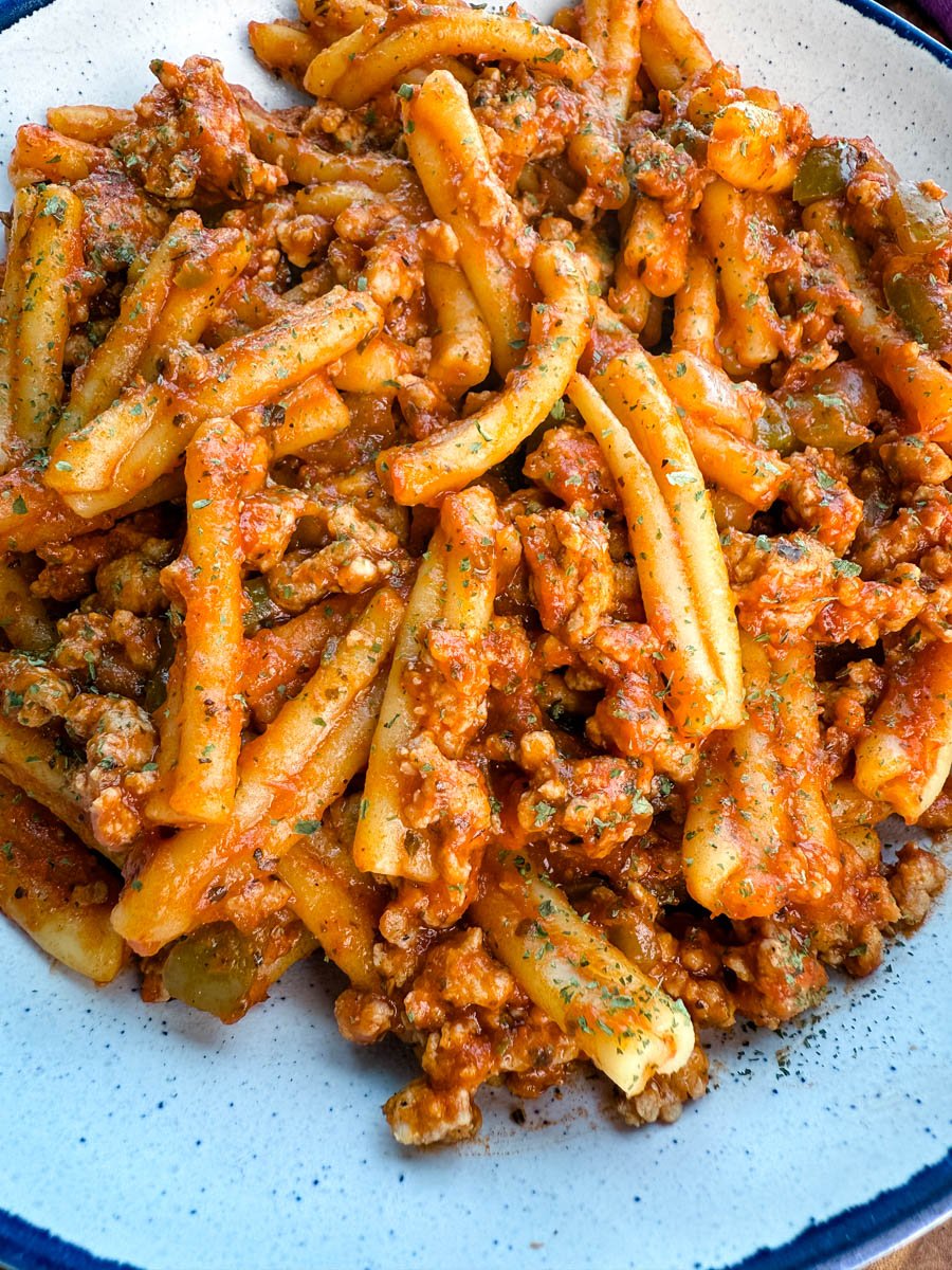 Close-up of the finished one-pot casarecce pasta tossed in a rich tomato sausage sauce, served in a speckled white bowl and sprinkled lightly with dried parsley.