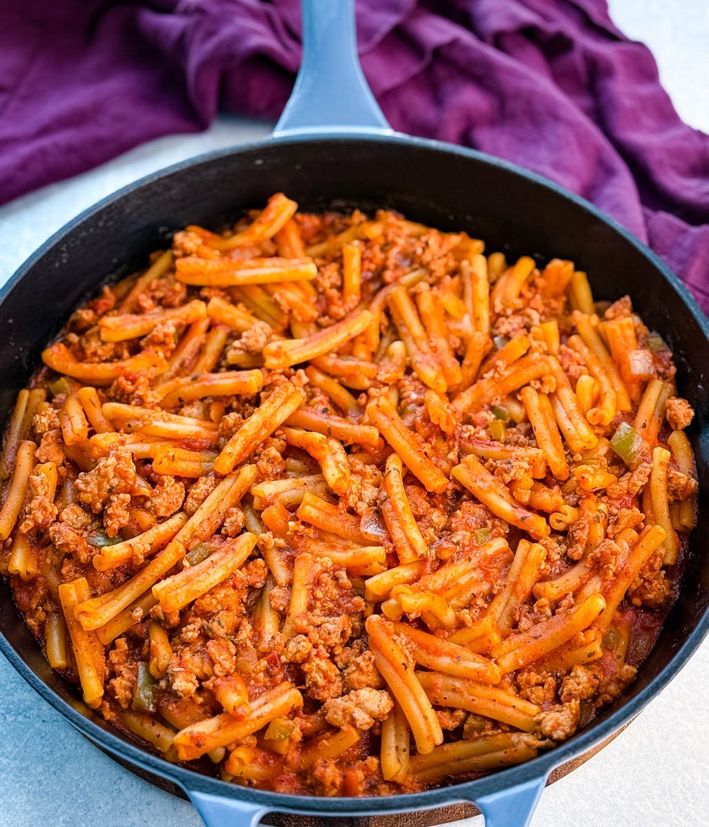 Cast-iron skillet shot of the completed one-pot pasta, noodles and sausage coated in a glossy tomato sauce, ready to serve straight from the pan.