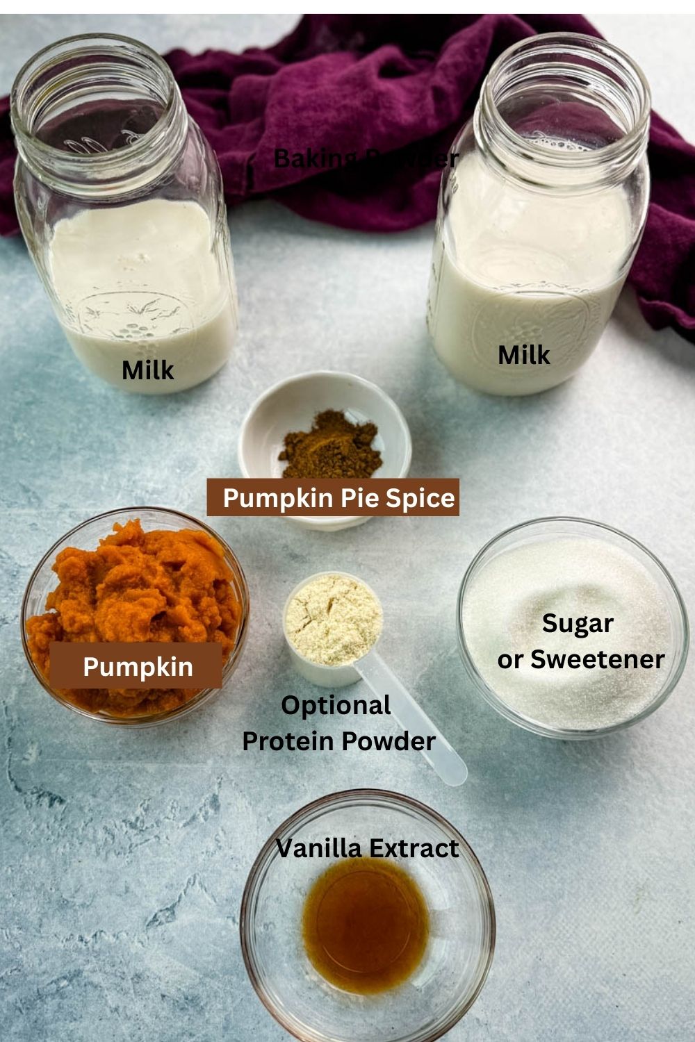 Overhead shot of milk, pumpkin puree, pumpkin pie spice, sugar, vanilla extract, and optional protein powder laid out in small bowls and jars on a light surface with a purple cloth.
